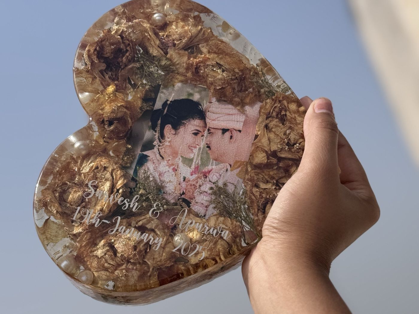 Preserved wedding flowers in a heart keepsake, held against the sky